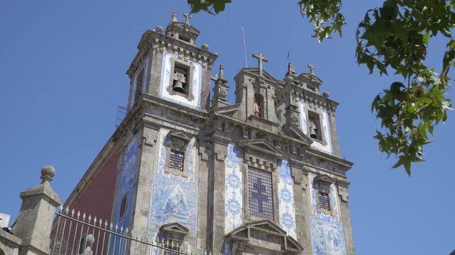 An upward view of the Church of Saint Ildefonso in Porto shows blue-and-white tile panels, twin bell towers and stone crosses.