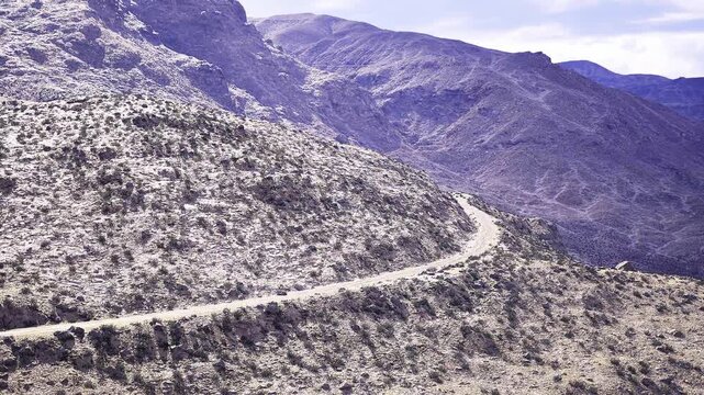 Winding dirt trail across rocky hillside, india highland panorama with dusty switchback road cutting through sparse scrub, sunlit slopes, muted tones, quiet