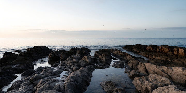 Rugged rocks and tide pools lead to a blue sea under a pale evening sky