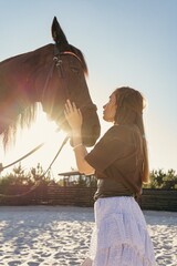 Horse. Horse and man. A woman hugs and touches a black horse in warm backlight on a sandy riding arena  a close-up portrait in profile. © Kateryna