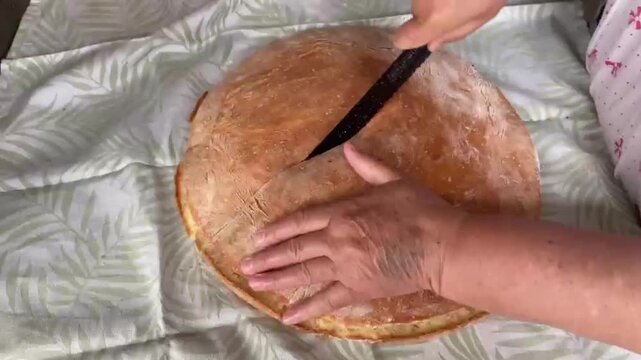 hands cut the crumb of hot semolina-flour bread with the big knife and turn the cloth