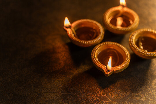 Four Traditional Clay Diwali Diyas with Flickering Flames Arranged on an Ornate Golden Patterned Surface, Warm Festive Close-Up Shot.