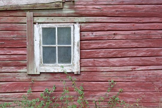 Rustic old wooden wall with traditional red paint and an aged window in the Swedish countryside.