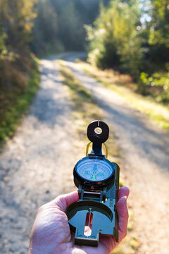 Hand holding military style compass while navigating forest trail. Outdoor navigation, wilderness orientation, hiking safety and adventure planning
