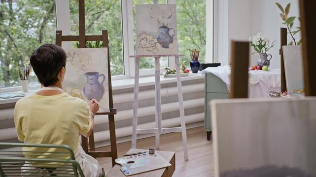 Senior Caucasian woman painting still life on easel from rear view during art class. Visual fits active aging, creative retirement, and art therapy projects