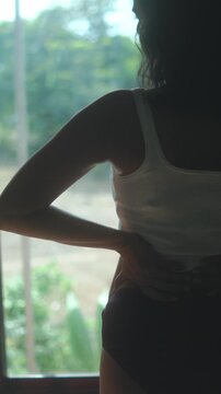 Woman in underwear stands by window, stretching in natural morning light indoors