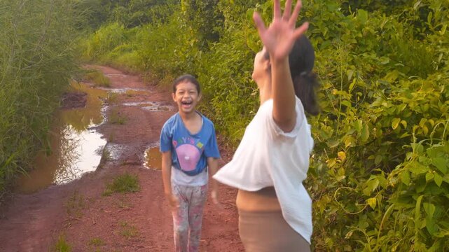 Woman and child raise and lower their arms while exercising together on a leafy rural path beside puddles for cheerful outdoor fitness and shared activity stories