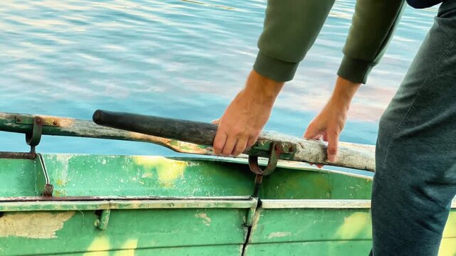Side view of a man hands detaching a wooden oar from an oarlock on a rowboat, suitable for fishing equipment ads, outdoor activity promos, and lake travel content.