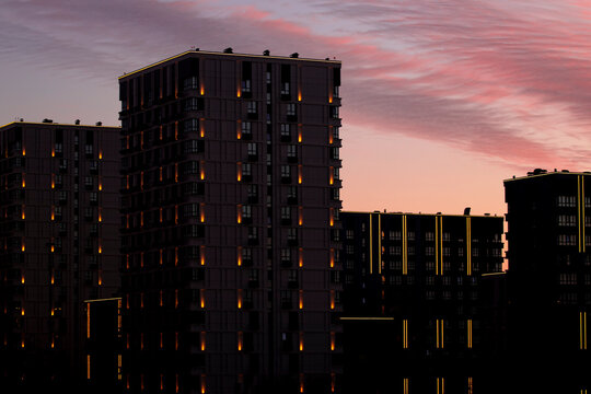 Glowing night city background with lights under dramatic sunset sky - urban lifestyle concept. Beautiful skyline view with modern dark building silhouette in atmospheric twilight evening.