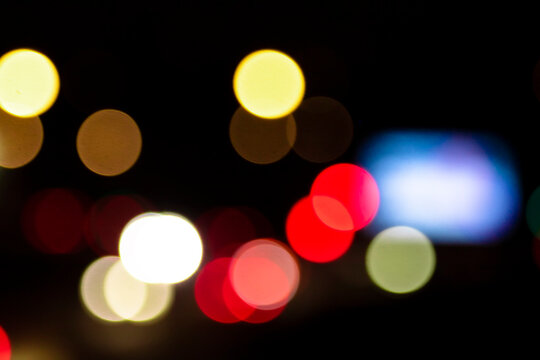 Bright night lights in city background with large bokeh &mdash; urban traffic transportation concept. Vibrant defocused evening road backdrop with glowing colorful circles. Abstract street movement.