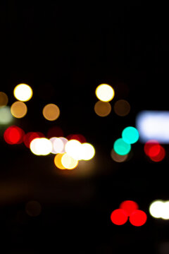 Vertical city background with abstract bokeh night lights &mdash; urban transportation commute concept. Colorful defocused glowing texture on dark street road. Vibrant atmospheric evening driving backdrop.