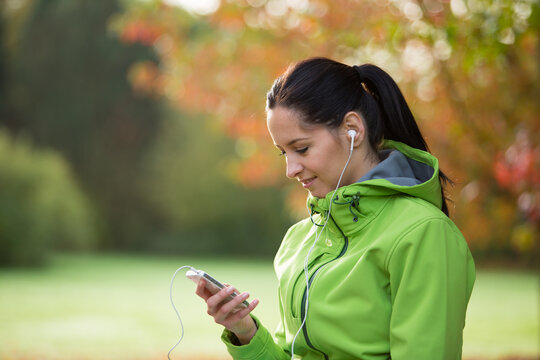 Woman Listening to Music with Headphones on a Park Bench in Autumn