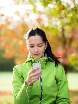 Woman Listening to Music with Headphones on a Park Bench in Autumn