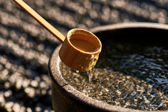 Bamboo water ladle pouring clear water over stone basin in serene garden, with warm morning sunlight, textured gravel, natural grain, and peaceful wellness atmosphere for zen meditation