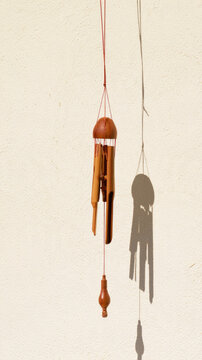 Bamboo wind chime hangs against pale stucco wall, casting delicate elongated shadow in warm sunlight, creating quiet minimalist mood with ample negative space for home decor design