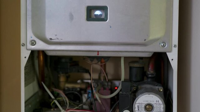 Open heating boiler showing internal components and illuminated indicator changing during visible error reset process in a close up home maintenance setting