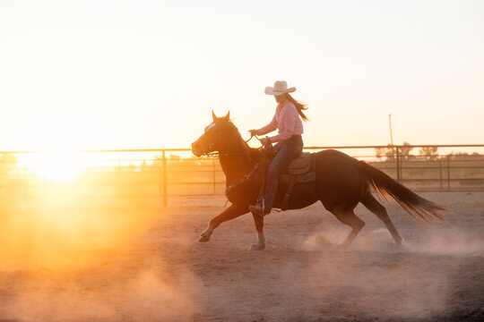Horse rider in cowboy hat in dusty outdoor arena at sunset