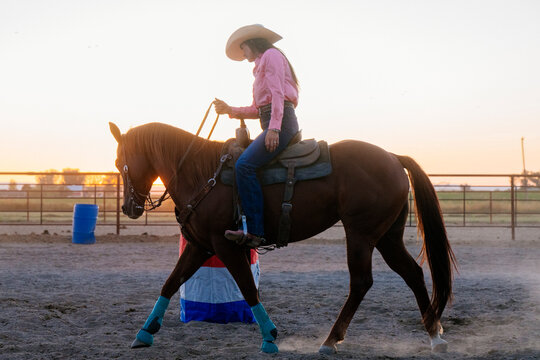 White woman riding horse in outdoor arena at sunset