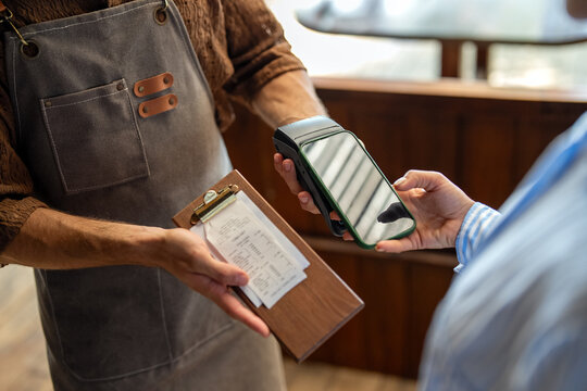 Female customer paying restaurant bill at the table through modern POS terminal