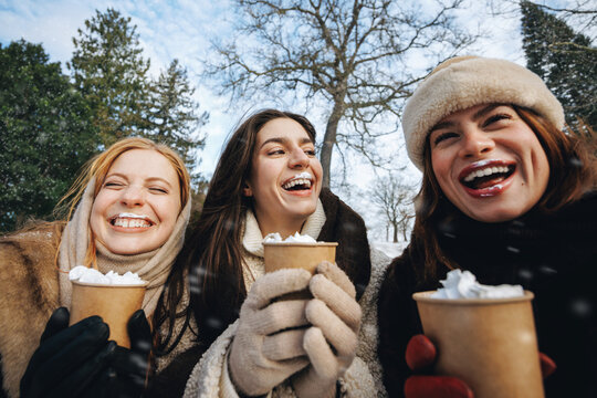 Women drink hot chocolate together outdoors in winter