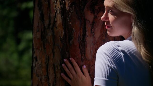 Woman gently touches ancient tree bark. Her eyes close, breathing softly. Sunlight breaks through forest canopy. She leans into nature's quiet strength. Ideal for eco, wellness, or mindfulness themes