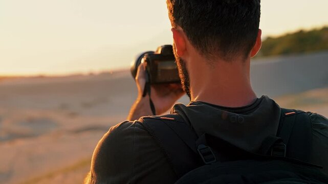 Close-up of a photographer capturing the sunset with a camera on the beach. Warm golden light highlights the moment in a striking coastal setting.