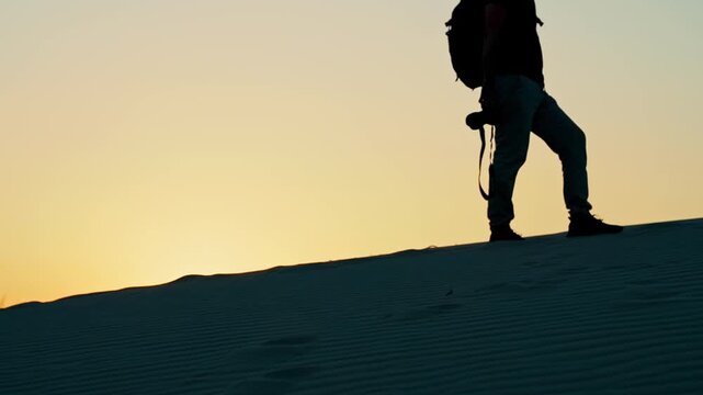 Silhouette of a photographer with a backpack at sunset, illuminated by reflected sunlight as the sun sinks toward the horizon.