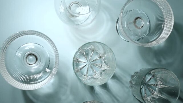 Assorted clear crystal glassware arranged on a light blue background with soft shadows