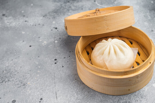Asian steamed bun in bamboo steamer on light surface, soft fluffy bao bread with filling and copy space.