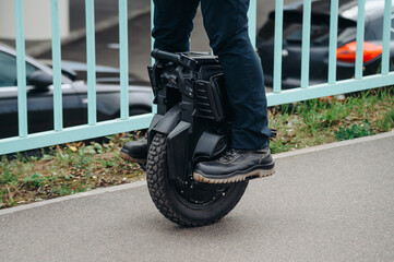 young man moving along sidewalk on unicycle in city park on embankment, unusual type of transport © Anton Pentegov