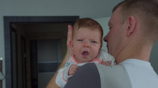 Dad supporting baby daughter head while holding her against his shoulder. Close-up of awake infant at home showing hands-on fatherhood and parental care