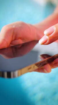 Close-up of female hands typing on a smartphone by a pool