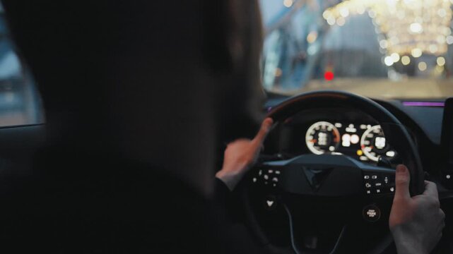 Backseat view on man driving car through the streets of the evening city.