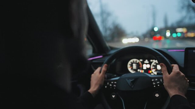 Backseat view on man driving car through the streets of the evening city.
