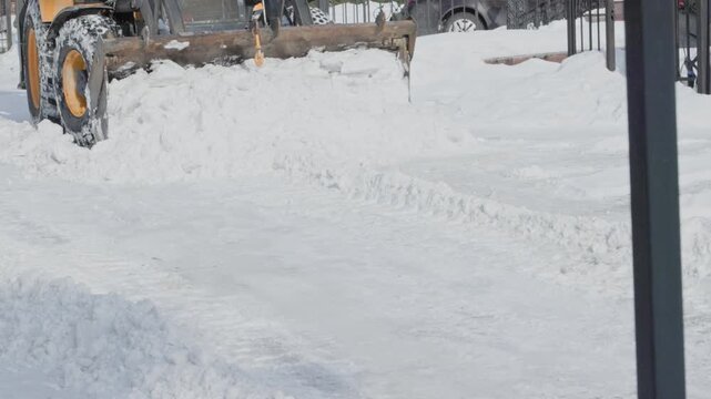 Wide view of a snow removal loader working across a residential driveway and opening a passable route through the snow covered yard.