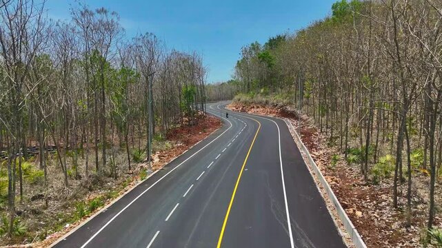Aerial view of a newly paved winding asphalt road to JLS cutting through dry deciduous hills during the dry season in Malang, East Java, Indonesia.