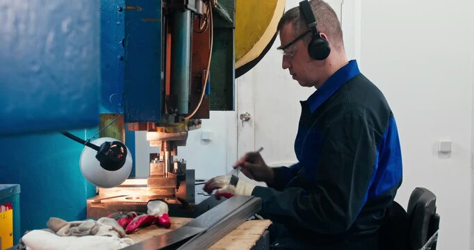 Blue collar factory worker operating stamping press for metal component bending. Industrial labor and component manufacturing, medium shot