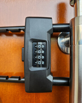 Close-up of a black 4-digit combination door lock mounted on a polished wooden door. Security mechanism with rotating number dials, sturdy design for home and office access protection. Modern saf