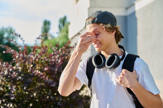 Young man squinting from bright sun and touching his face outdoors on sunny day