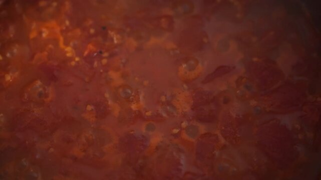Overhead close-up of boiling tomato pulp in a metal pot on the stove. Sauce bubbles and tomato chunks clearly visible. Idea of homemade pizza sauce and natural tomato cooking