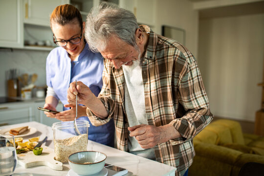 Senior man weighing oats while woman checks phone in kitchen