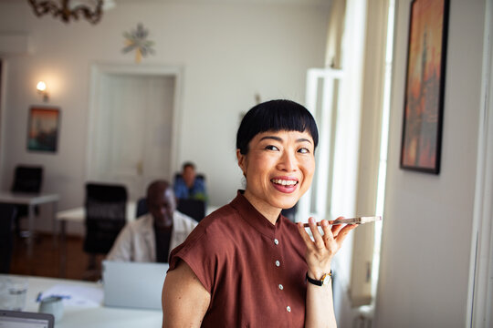 Smiling woman using voice command on smartphone in office