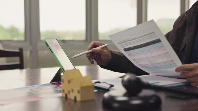 Lawyer analyzes mortgage documents beside digital tablet, gavel, house model at office desk. Foreclosure auction process, property law adjudication, real estate dispute litigation settlement.