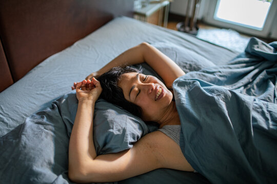 Smiling woman waking up and stretching in bed