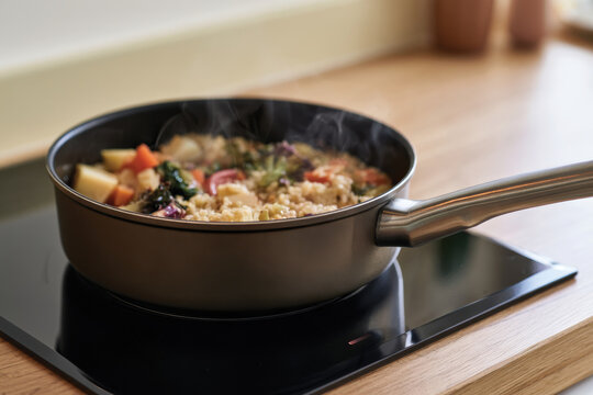 A vibrant vegetable dish simmering in a black frying pan atop a stylish stove, releasing steam and showcasing fresh ingredients and home cooking artistry.