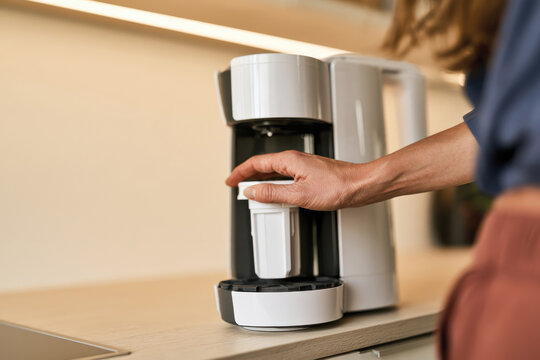 A hand is poised to operate a sleek coffee maker, emphasizing modern convenience and daily rituals of brewing coffee in a stylish kitchen environment for personal enjoyment.