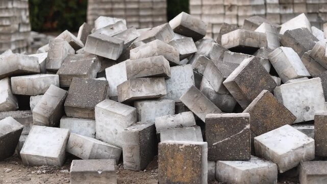 Paving tiles are haphazardly scattered across construction area during sidewalk repairs. Messy storage reveals careless handling and lack of workplace discipline.