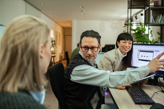 Man points at monitor while discussing presentation with team
