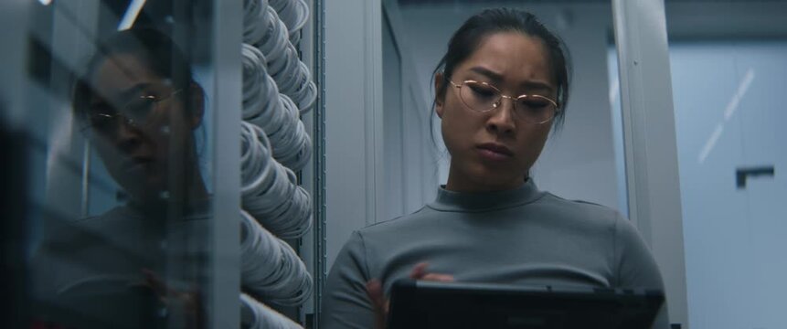 Female Checks Cable Connections and Reviewing System Data on Tablet. Focused Expression Suggests Technical Diagnostics, Server Infrastructure Assessment, and Enterprise Network Performance Monitoring.