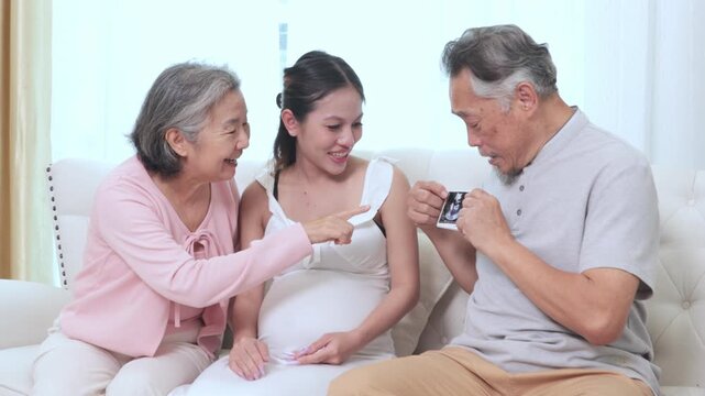 Elderly couple clearly doting beautiful pregnant daughter who is nearing due date sit happily looking at an ultrasound scan they share joy eagerly await the arrival grandchild due in just few months.